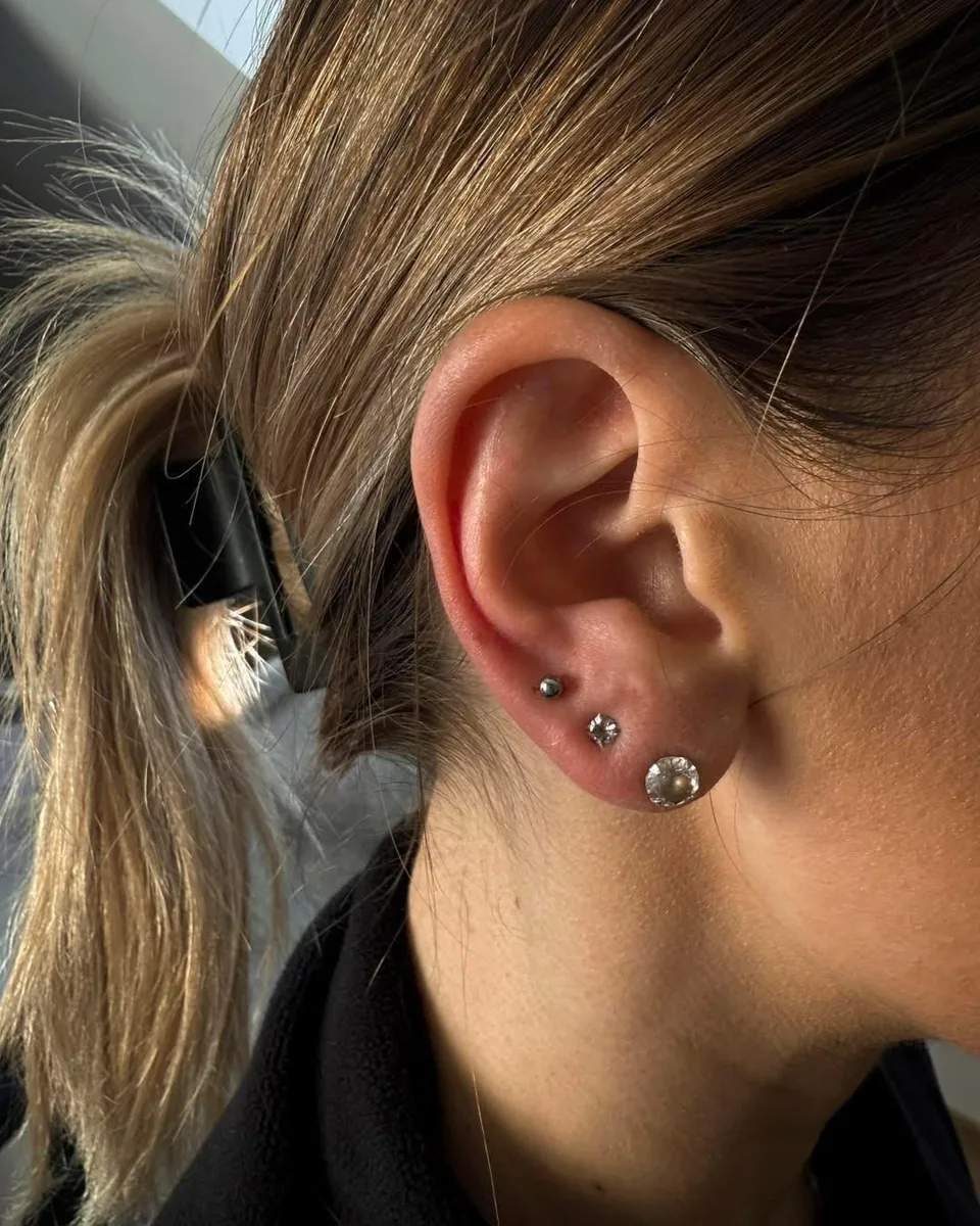 Świeże przekłucia płatka ucha – trzy kolczyki z cyrkoniami ułożone rosnąco, zbliżenie ucha – piercing Martyny, SHADY TATTOO Wieluń
