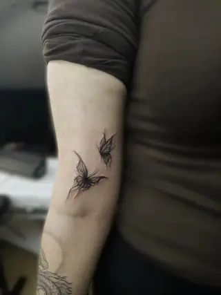 Dwa czarne motyle wykonane cienką kreską na wewnętrznej stronie przedramienia – tatuaż Zuzi, SHADY TATTOO Wieluń